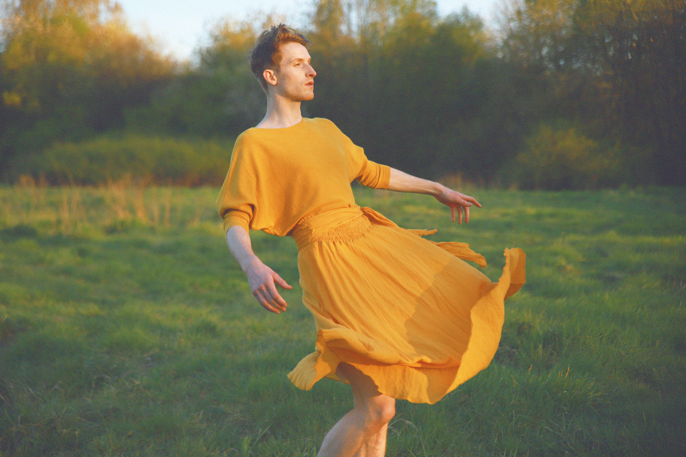 Person in a green meadow wearing long yellow dress that is caught by the wind.