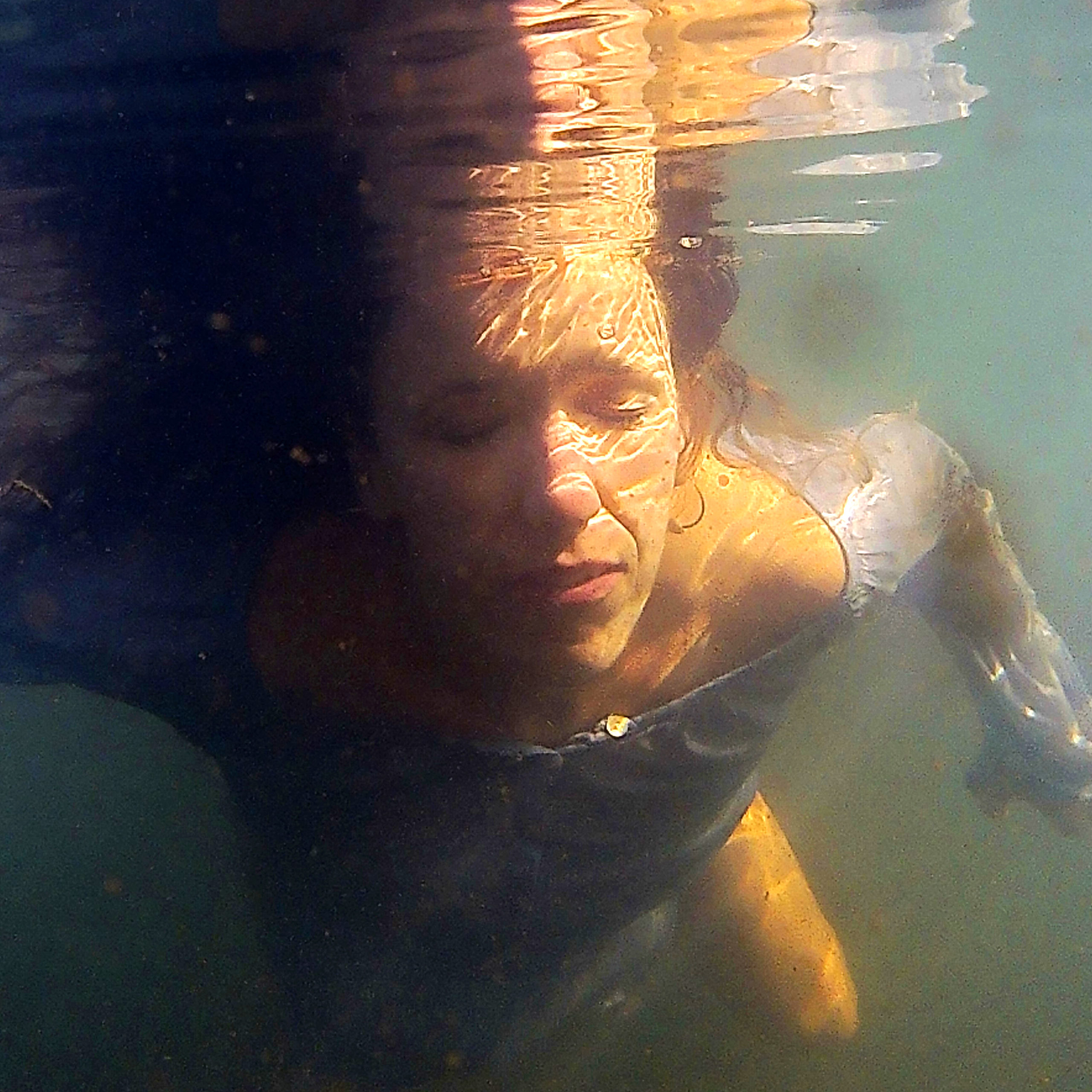 Woman captured underwater with eyes closed wearing a blue shirt.